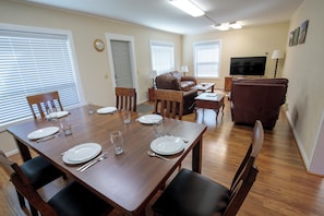 A dining area with a wooden table set for four, a brown leather sofa, and a television in the background.