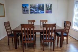 A dining area with a wooden table and six chairs, three on each side. There are three framed pictures on the wall above the table. - Walk to Downtown • King Bed • Near Olympic Beaches (Forks)