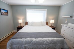 A bedroom with a bed, two bedside tables with lamps, a dresser, and a window with blinds. - Walk to Downtown • King Bed • Near Olympic Beaches (Forks)