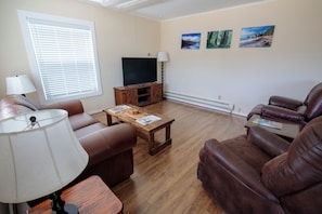 A living room with a flat-screen TV, leather sofas, a wooden coffee table, and a window with blinds. - Walk to Downtown  • King Bed • Near Olympic Beaches (Forks)