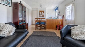 A living room with a black leather sofa, a wooden chair, a cabinet, and a kitchen area with a microwave and a fire extinguisher. - 2 Bed Chalet - Sleeps 4 - River and mountain views (Strathpeffer)