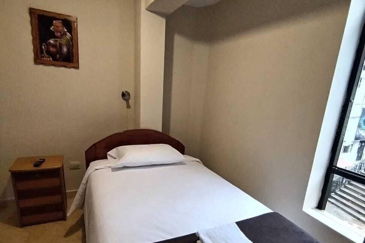 Une chambre à coucher avec un lit, une table de chevet, une fenêtre et un tableau accroché au mur.