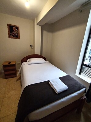Un dormitorio con cama, mesita de noche, ventana y un cuadro en la pared.