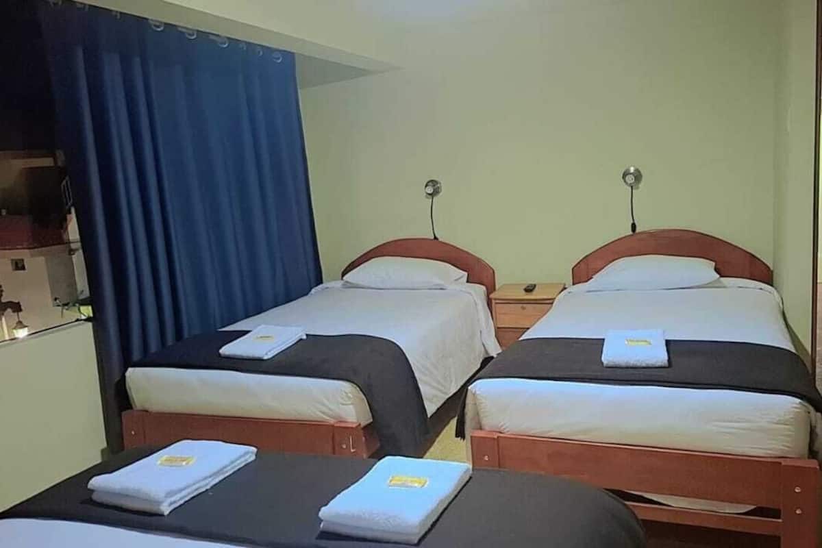 Une chambre avec deux lits, chacun doté d’une tête de lit en bois et de linge de lit blanc. On y trouve une petite table sur laquelle sont posés une serviette pliée et une télécommande.