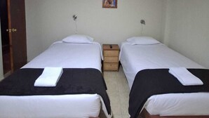 Una habitación pequeña y limpia con dos camas individuales, una mesita de noche de madera, una pequeña mesa y una puerta.