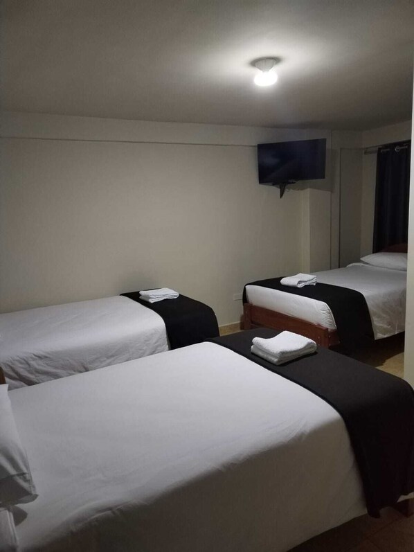 A hotel room with two single beds, a flat-screen TV mounted on the wall, and a ceiling light.