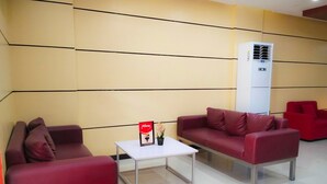 Un área de espera moderna con sofás rojos, una mesa de centro blanca y un atril para menús.