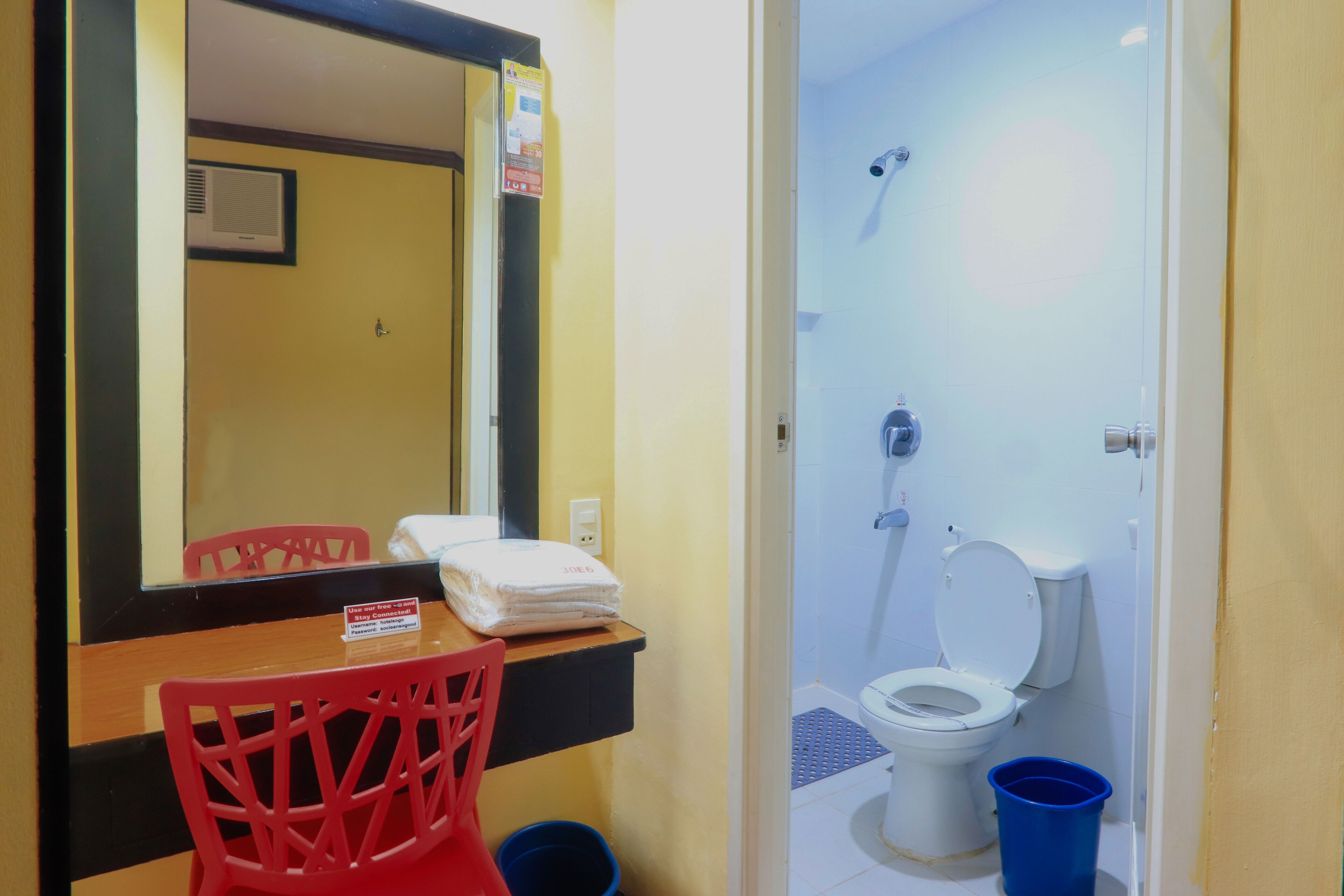 A bathroom with a toilet, a sink, a mirror, and a red chair.