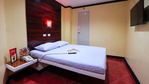 Una habitación de hotel con una cama, una mesita de noche con un teléfono, un televisor montado en la pared y una puerta.