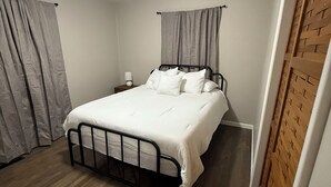 A bedroom with a bed, curtains, a nightstand, and a wooden floor.