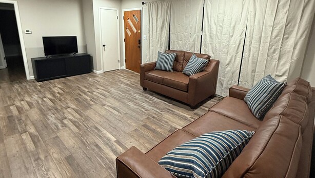 A modern living room with a brown leather sofa, a smaller brown sofa, and a TV on a stand.