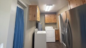 A compact kitchen with wooden cabinets, a washing machine, a refrigerator, and a ceiling light.