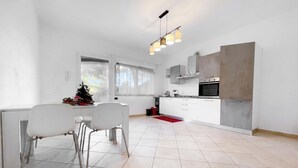 A modern kitchen with white cabinets, a built-in oven, and a dining area with two chairs and a table. - Miramare 3 LUX - Total Sea View, Andora, Italy (Andora)