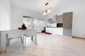A modern kitchen with white cabinets, a built-in oven, and a dining area with two chairs and a table. - Miramare 3 LUX - Total Sea View, Andora, Italy (Andora)
