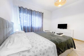 A bedroom with a bed, a television, and a window with curtains. - Miramare 3 LUX - Total Sea View, Andora, Italy (Andora)