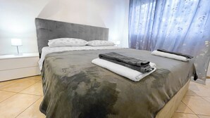 Et moderne soveværelse med en stor seng, en grå sengegavl og et natbord med en lampe.