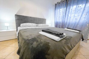 Een moderne slaapkamer met een groot bed, een grijs hoofdeinde en een nachtkastje met een lamp.