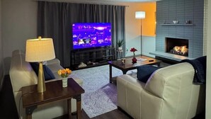 Una sala de estar con una televisión de pantalla plana, un sofá, una mesa de centro, una lámpara, una chimenea y una alfombra.