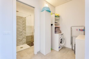 A compact laundry room with a washing machine, a drying rack, and a shower area. - Miramare 1 LUX - Total Sea View, Andora, Italy (Andora)