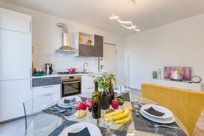 Een moderne keuken met witte kasten, een inbouwoven en een eethoek met een glazen tafel gedekt voor twee personen.