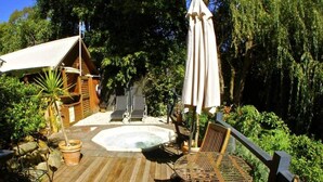 Une terrasse en bois avec un jacuzzi, des sièges d’extérieur et une petite structure en bois.