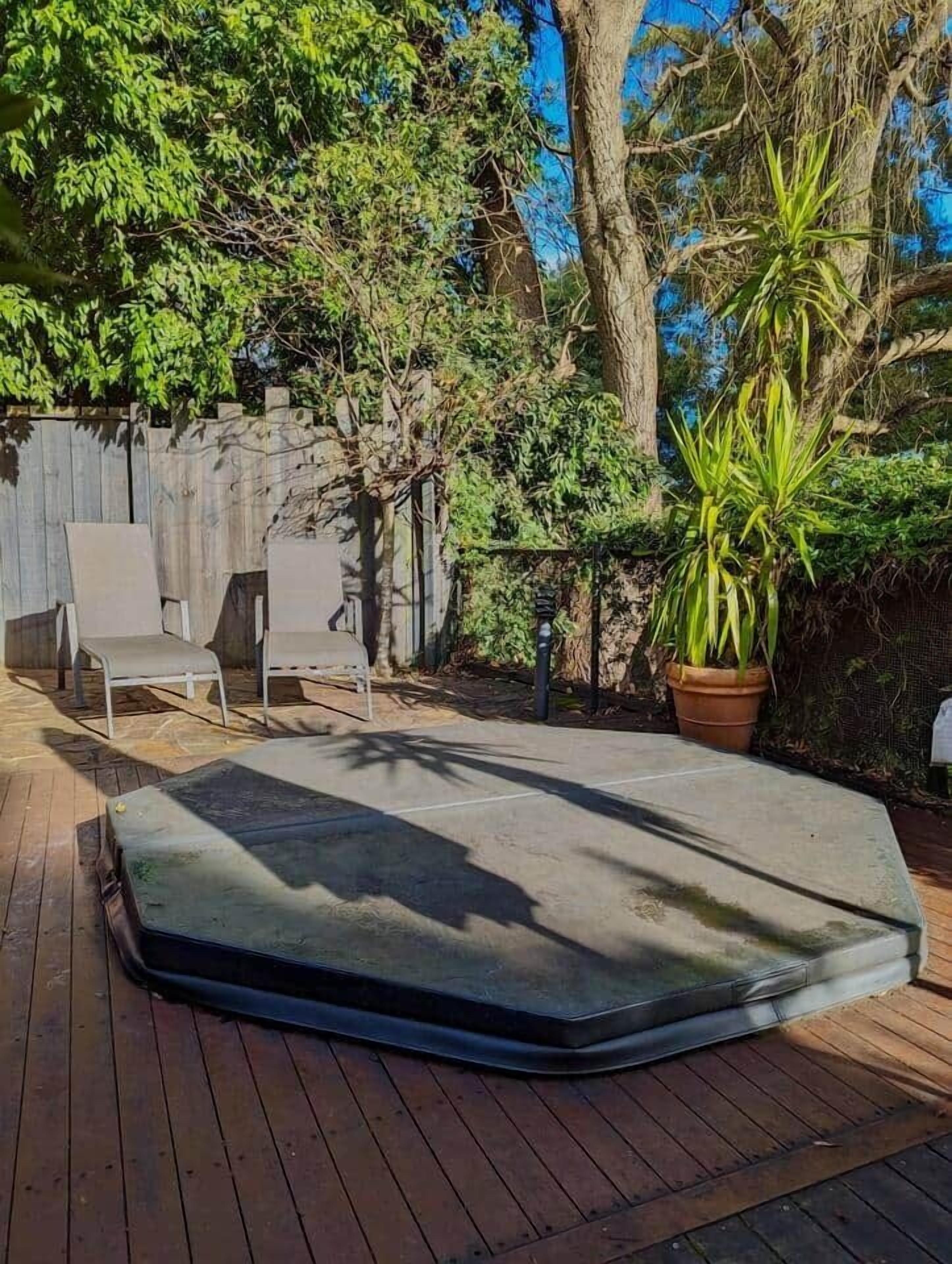 Une terrasse en bois avec un matelas, deux chaises blanches et une plante en pot.