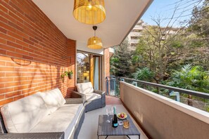 Un balcone con mobili in vimini, una bottiglia di vino e un bicchiere su un tavolo.