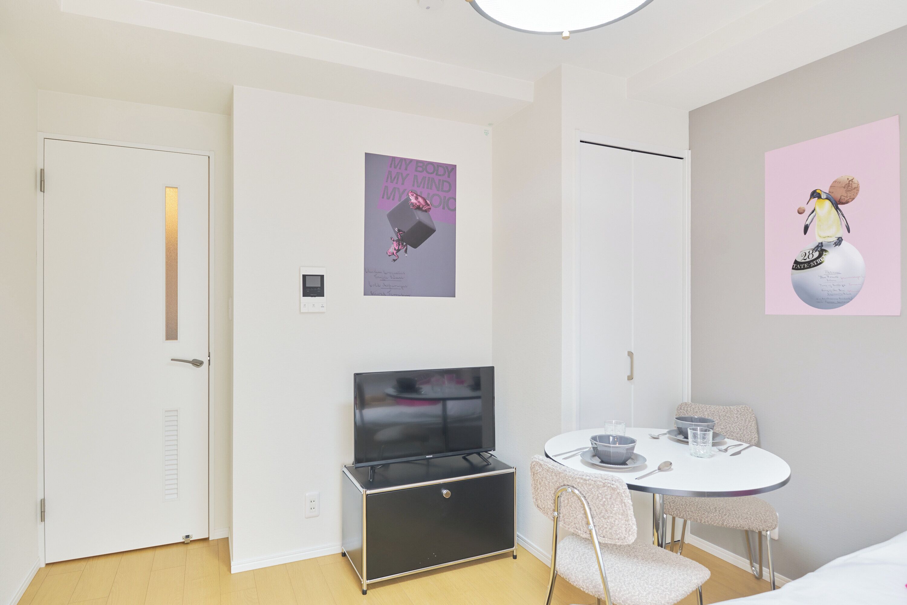 Habitación de hotel con televisión, una mesa de comedor con sillas, un cartel en la pared y una puerta.