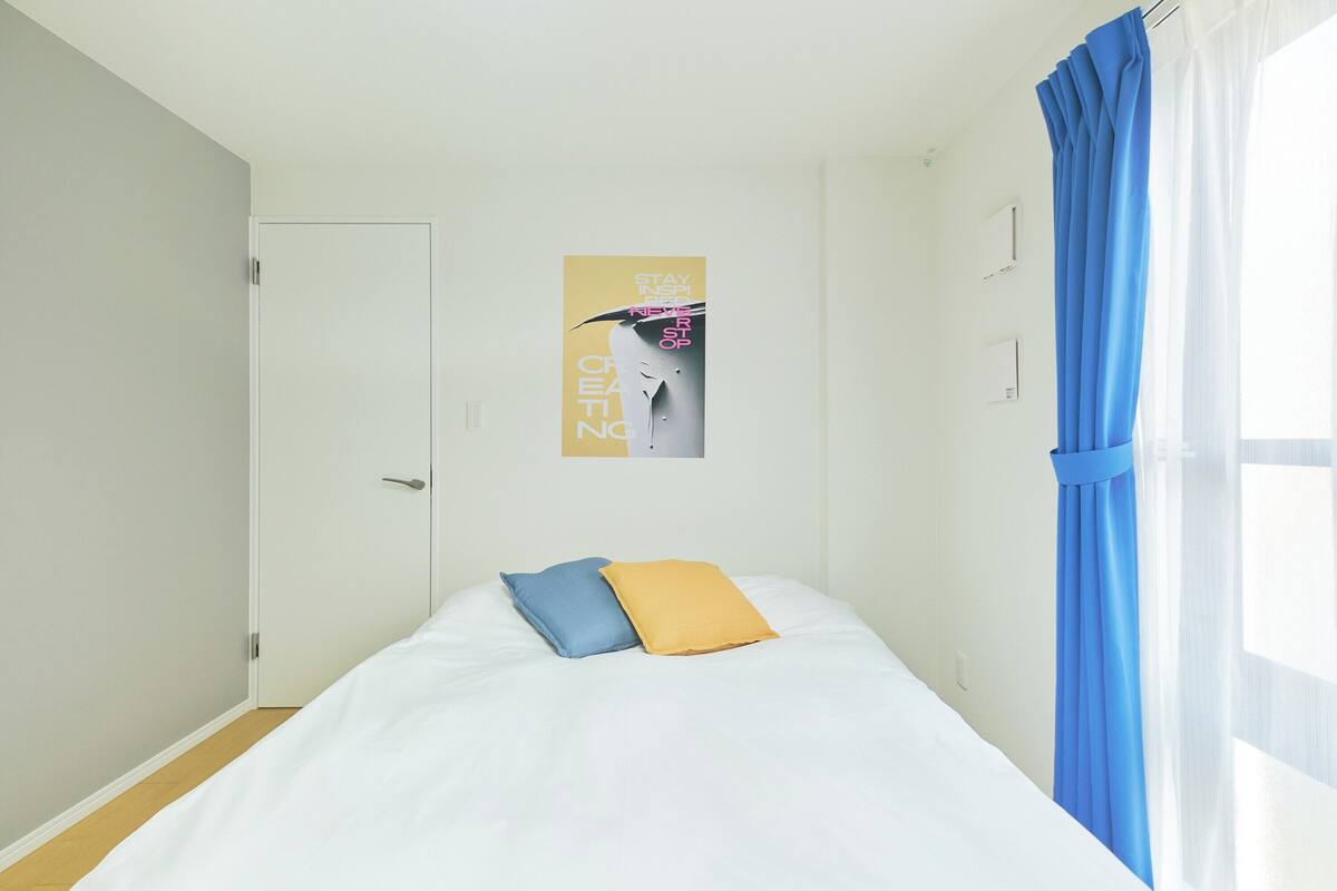Un dormitorio con cama, dos almohadas, un cartel y una ventana con cortinas.
