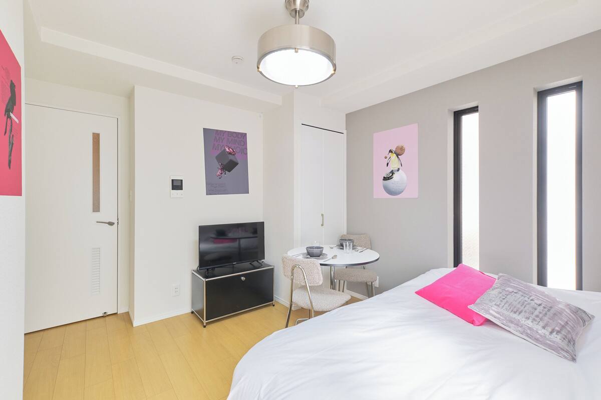 Una habitación de hotel moderna con una cama, un televisor, una mesita redonda pequeña y una silla.