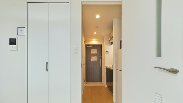 Un couloir étroit doté d’un plancher en bois, de murs blancs et d’une porte donnant sur un espace cuisine.