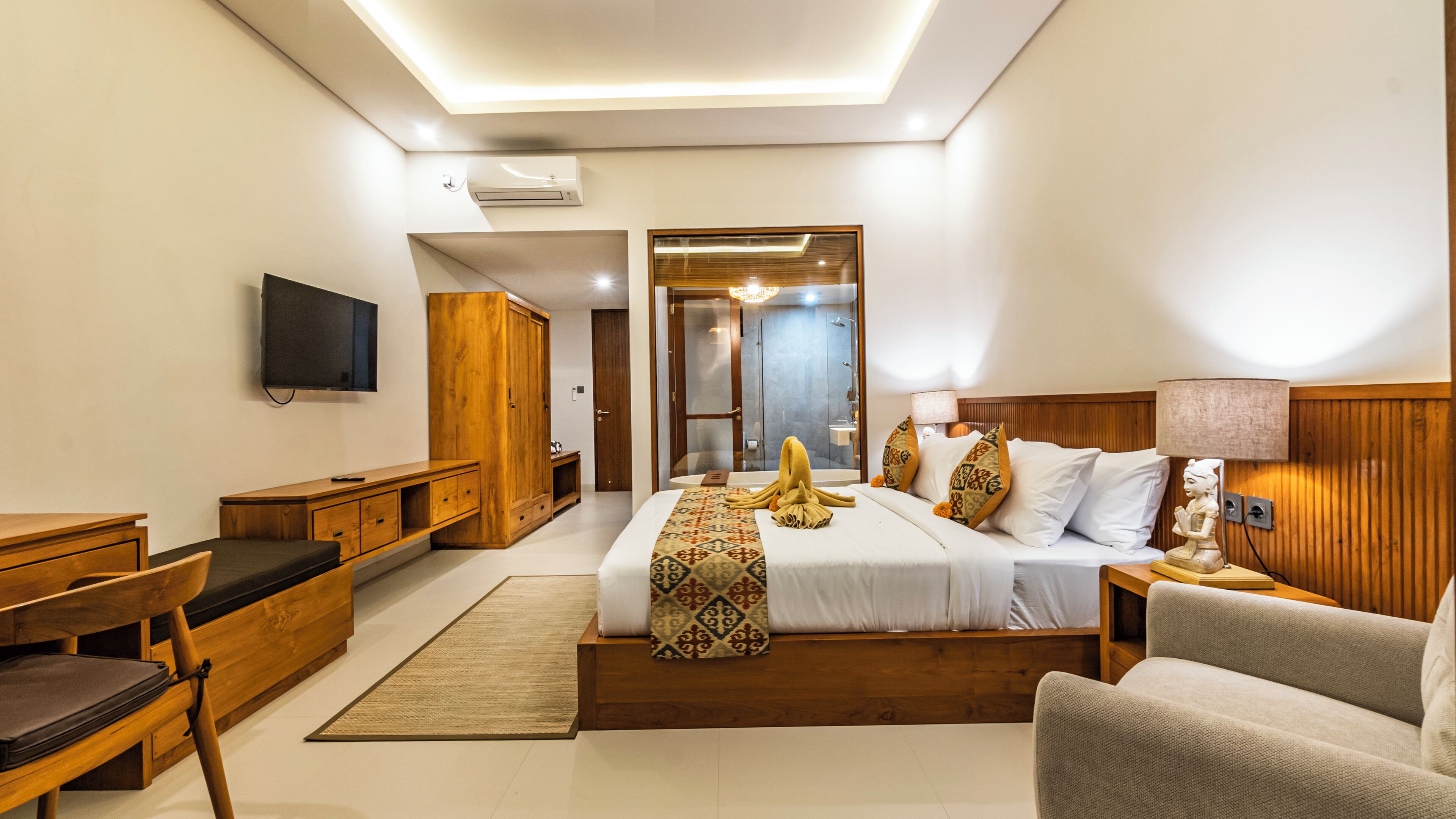 A modern hotel room with a large bed, a desk, a chair, a TV, and a shower area.