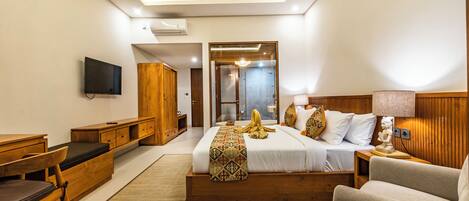 A modern hotel room with a large bed, a desk, a chair, a TV, and a shower area.