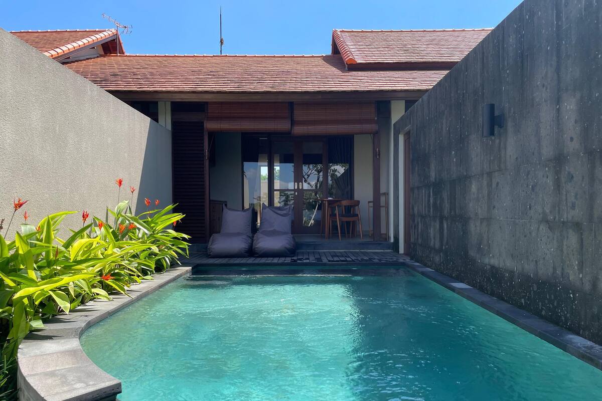 Ein Pool mit gewölbter Kante, umgeben von einer Betonmauer und einem Ziegeldach.