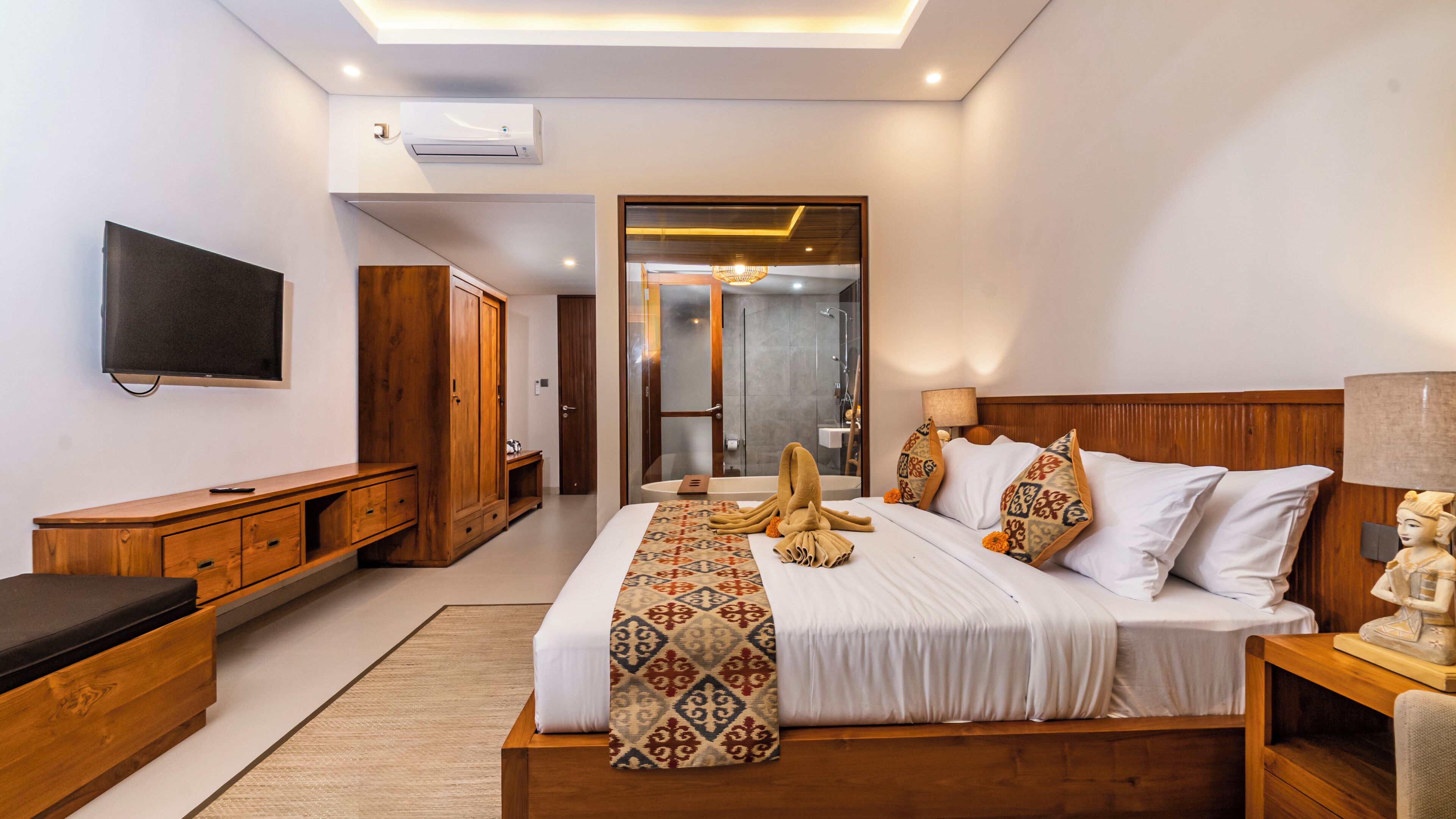 A modern hotel room with a large bed, wooden furniture, a flat-screen TV, and a walk-in shower.