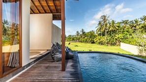 A wooden deck with a pool, a white wall, and a view of a lush green landscape with palm trees. - Sabuh Mas Villa Ubud By Aswanaya (Tegallalang)