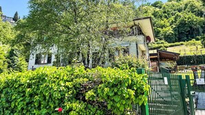 A building with a white facade and multiple windows, surrounded by lush greenery and a hill in the background. - Beautiful apartment for 5 people with WIFI, TV, patio and pets allowed (Perledo)