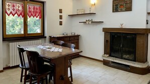 A dining room with a wooden table and chairs, a fireplace, and a window with lace curtains. - Beautiful apartment for 5 people with WIFI, TV, patio and pets allowed (Perledo)