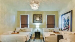 Ein Hotelzimmer mit zwei Betten, einer Chandelüstere, Bildern an der Wand und einem kleinen Tisch mit Tablett.