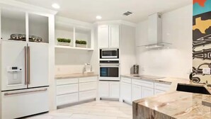 Una cocina moderna con armarios blancos, horno empotrado y encimera de mármol.