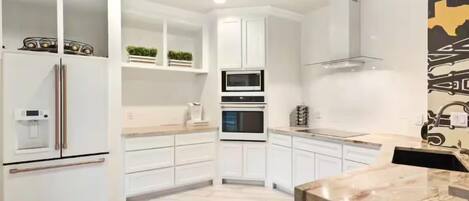 Una cocina moderna con armarios blancos, horno empotrado y encimera de mármol.