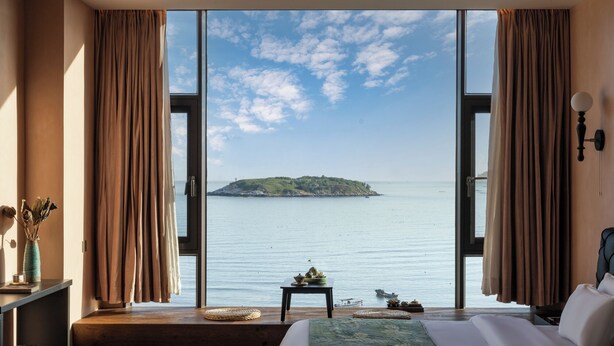 Ein Schlafzimmer mit großem Fenster, das auf ein ruhiges Meer und eine kleine Insel Blick bietet.