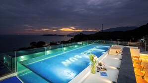 Ein Dachpool mit Infinity-Kante und Blick auf das Meer und die Berge bei Sonnenuntergang.