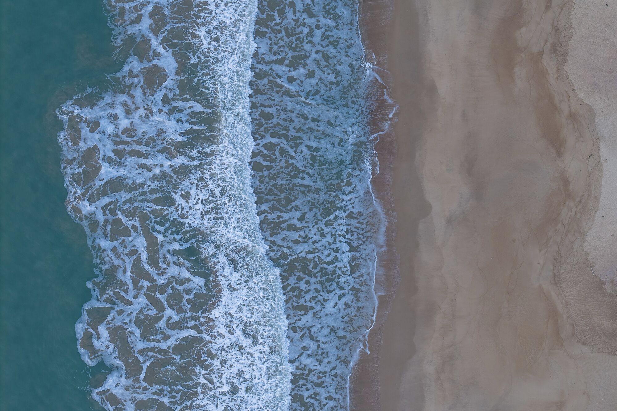Vista aérea de uma praia com ondas quebrando na costa.