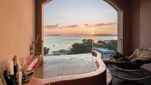 Ein Balkon mit Whirlpool, einem Korbstuhl und Blick auf den Sonnenuntergang über dem Meer.