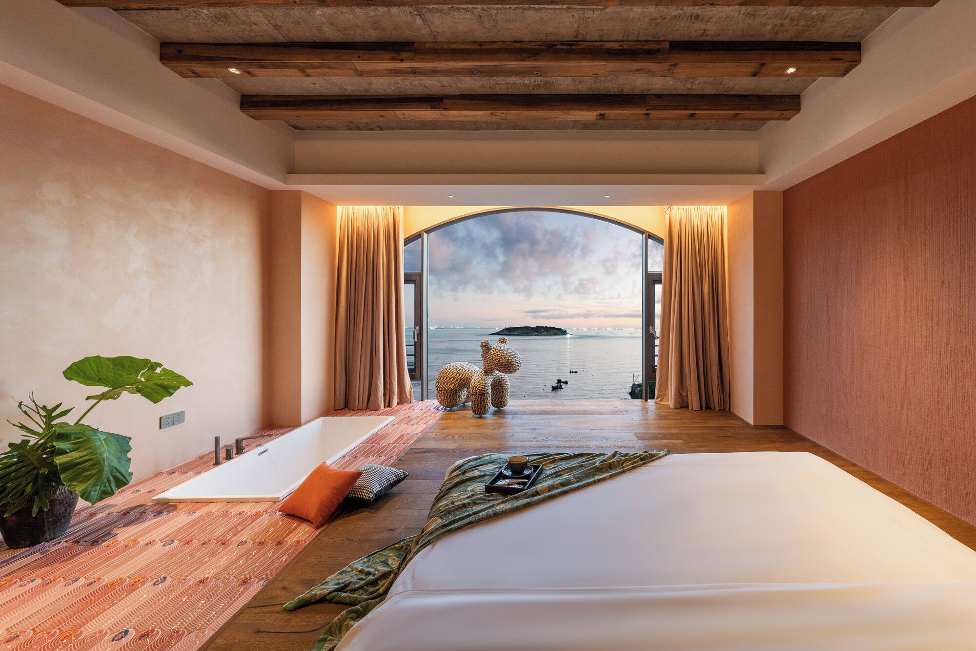 A bedroom with a large bed, a bathtub, and a view of the sea.
