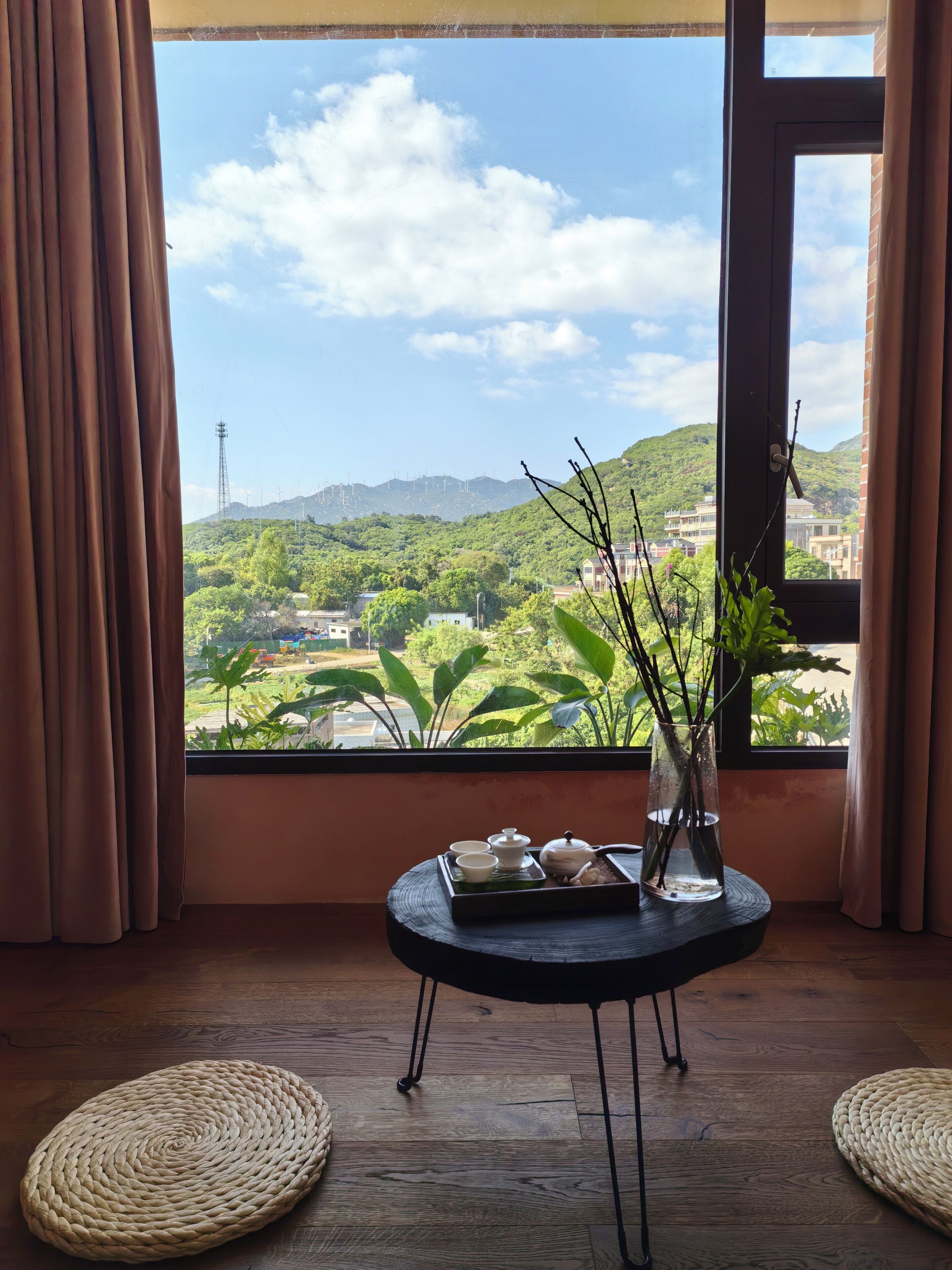 A room with a view of a green landscape and mountains. There is a small table with a vase and a tray of items.