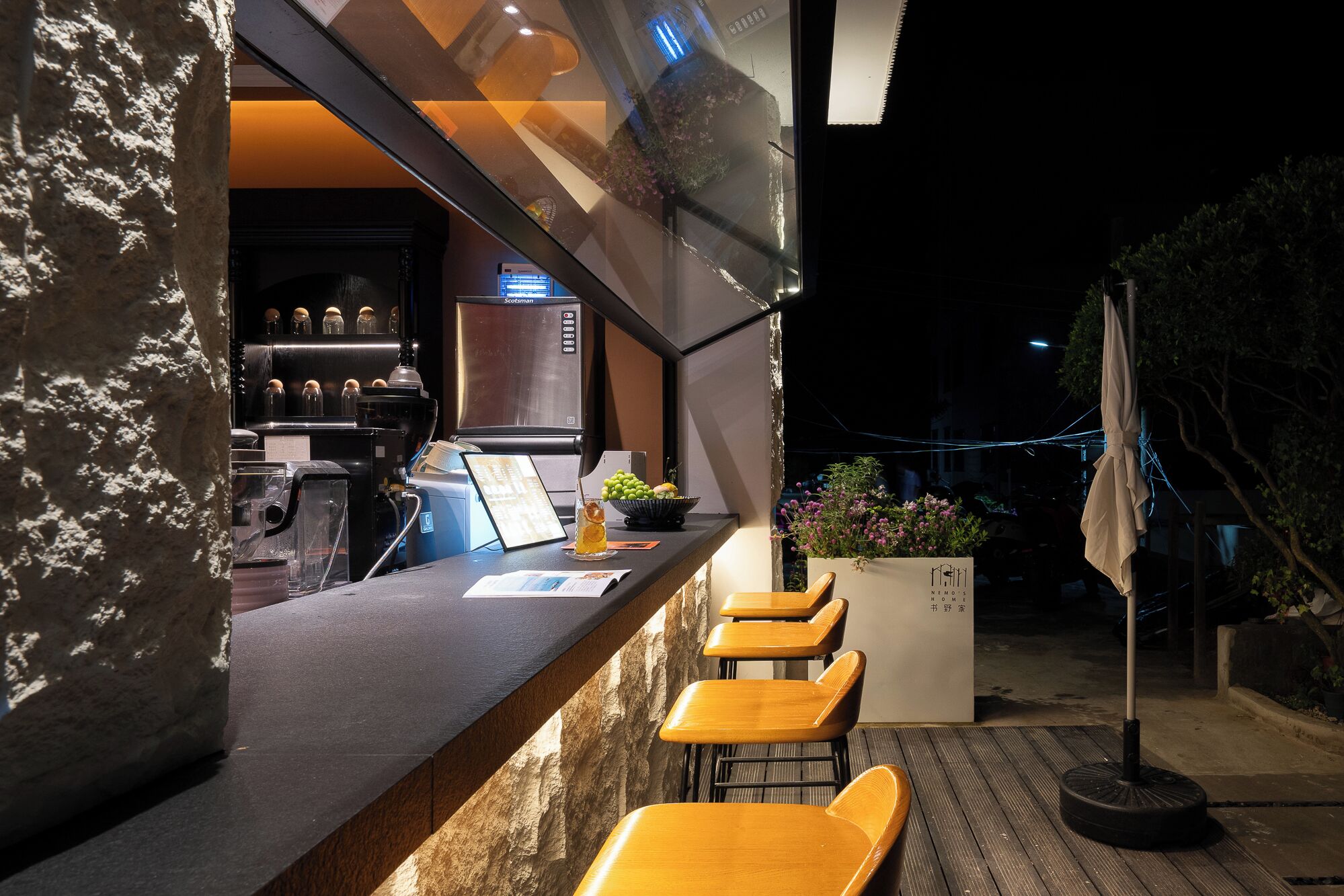 A bar area with a stone counter, bar stools, and a refrigerator.