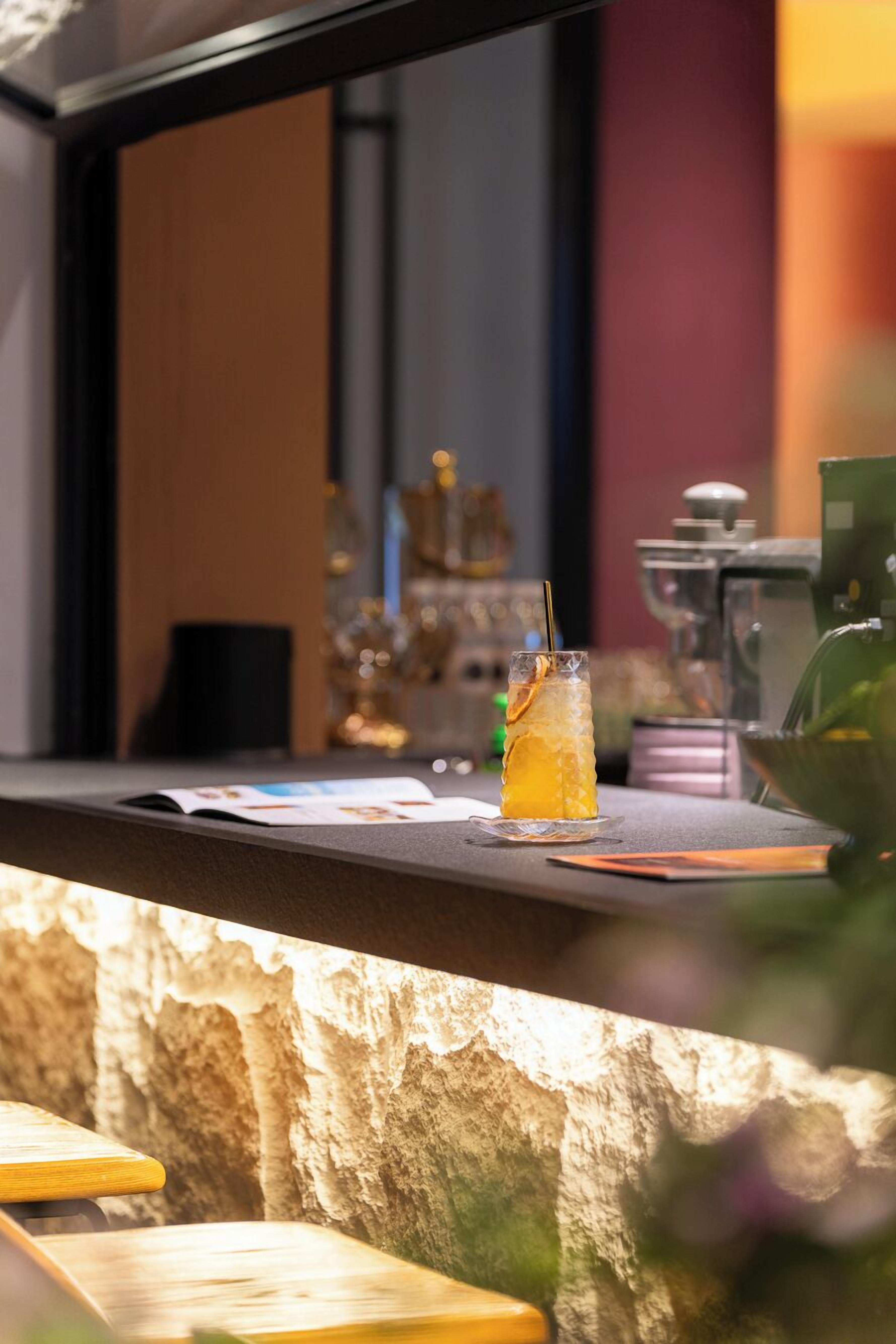 A bar area with a glass of iced drink, a menu, and a coffee machine.