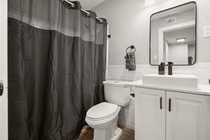 A bathroom with a toilet, sink, mirror, and shower curtain. - Crestview Suite | Super Close to Downtown Austin (Austin)